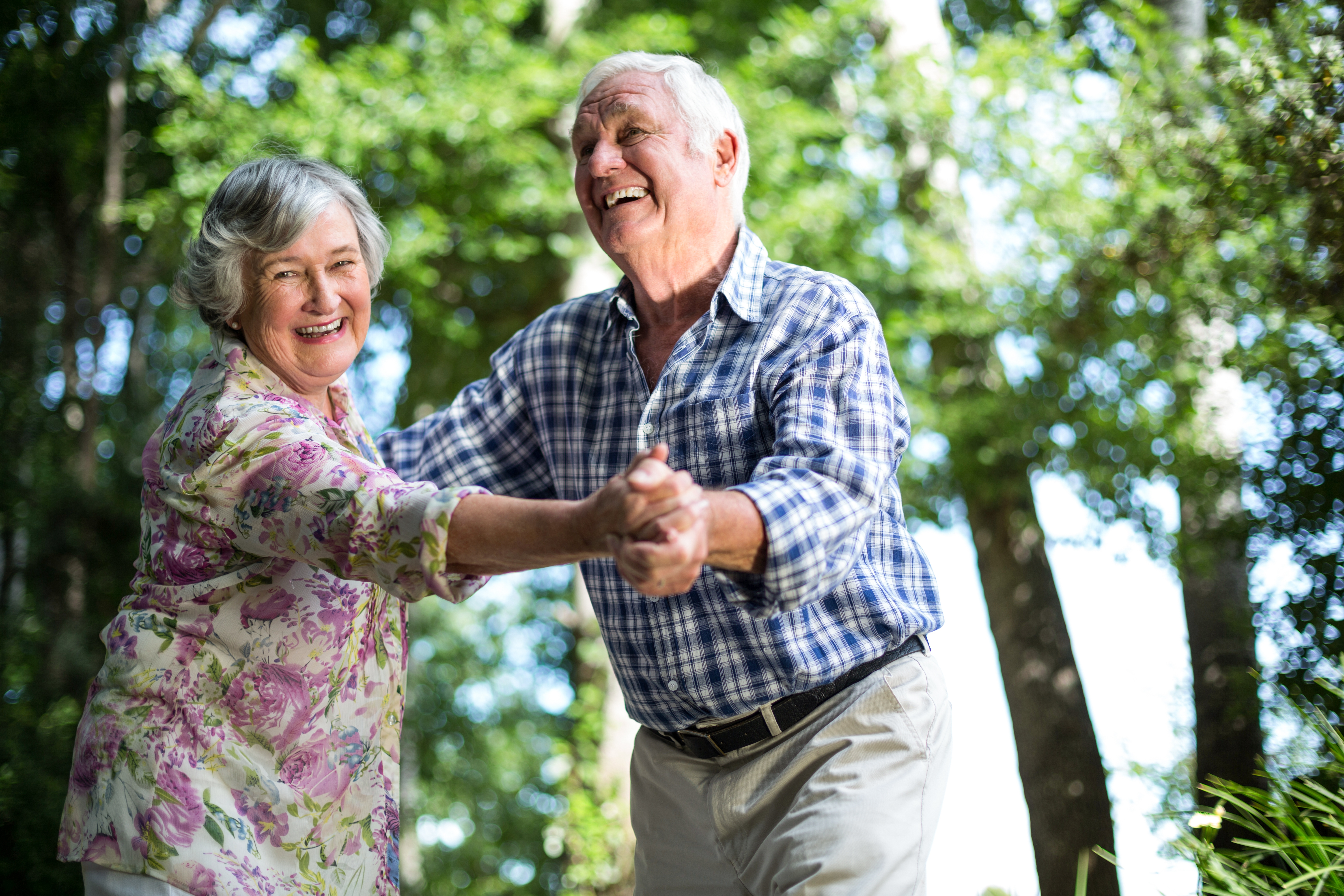 Happy senior woman dancing with husband against trees