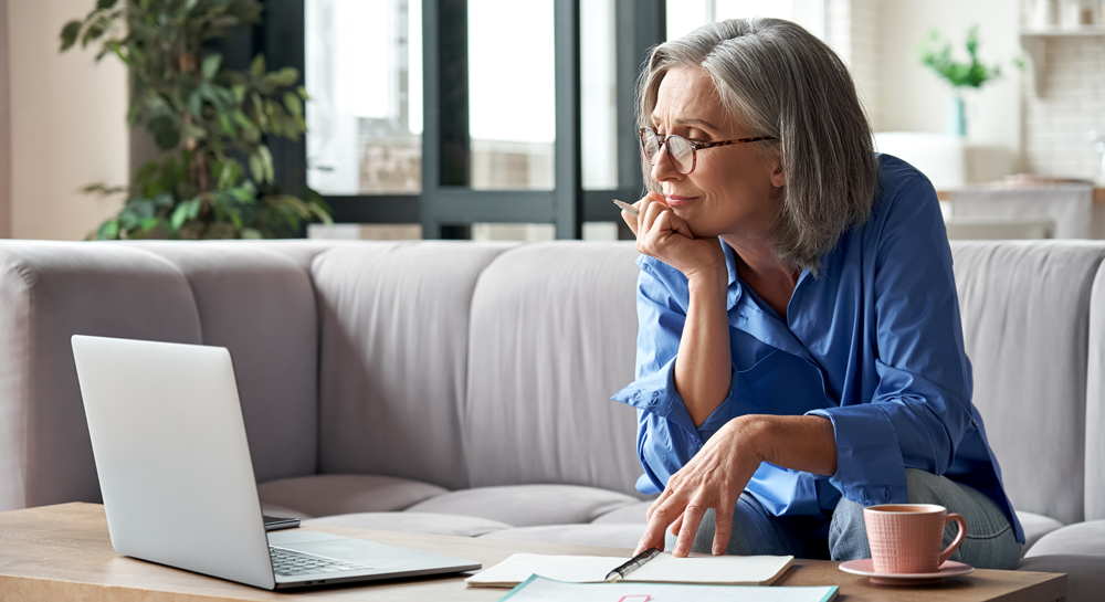 Woman over 65 sitting on her couch at home looking for Medicare on her laptop.